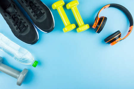 Fitness equipment. Sneakers, water, dumbbells and headphones on blue backgroundの写真素材