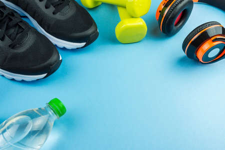 Fitness equipment. Sneakers, water, dumbbells and headphones on blue backgroundの写真素材