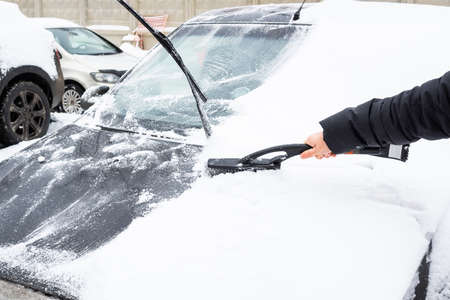 Removal snow from car body with brush, man cleans the car from snow after snowfall