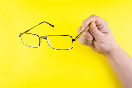 Men's hand holding glasses on yellow backgroundの写真素材