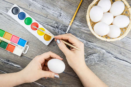 White eggs, paints, tassels, preparation for coloring for Easter. Women's hands paint eggs for Easterの写真素材