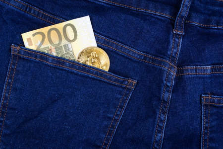 Bitcoin cryptocurrency in the pocket of blue jeans and Euro banknotesの写真素材
