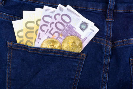 Bitcoin cryptocurrency in the pocket of blue jeans and Euro banknotesの写真素材
