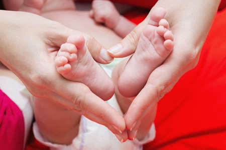 Newborn baby feet in mother hands, shape like a lovely heart. Mother holding legs of the kid in hands. Close up image. Happy family concept.の写真素材