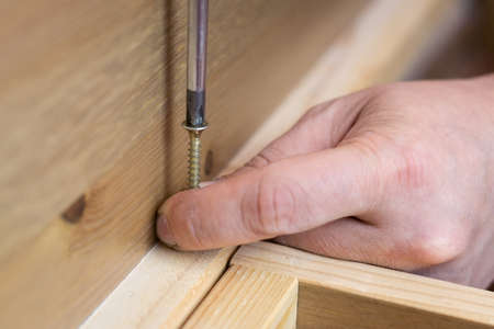 Assembling wooden furniture, using a wireless screwdriver, close-up