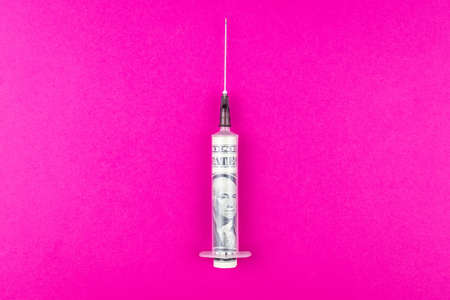 Dollars and medical syringe are lying on a pink background. The concept of dependence on the dollar.