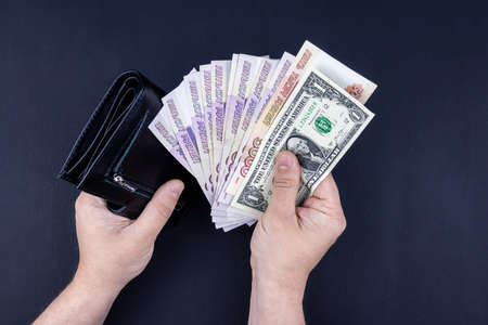 A man is holding an open wallet with money in his hands. Hands take out bills from his wallet. The...