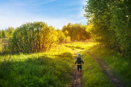 Cute little baby boy walks through the summer park. Child is laughing. Adorable baby boy in a blue sweatshirt. Happy child in the forest.の写真素材