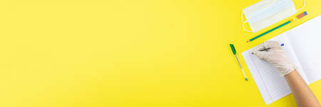 Child writes on a notebook in a rubber glove and medical mask, but at school he covid-19. Photo...