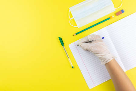 Child writes on a notebook in a rubber glove and medical mask, but at school he covid-19. Photo...