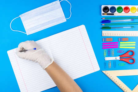 Child writes on a notebook in a rubber glove and medical mask, but at school he covid-19. Photo...