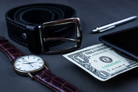 Men fashion and accessories, Wrist watch with black leather strap on with a ballpoint pen, and a dollar in my wallet a black backgroundの写真素材