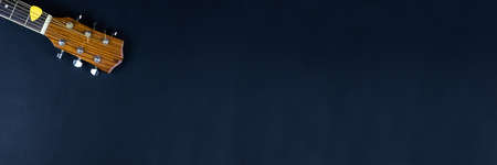 yellow guitar pick tucked into gold acoustic guitar strings on a dark wood fret board.の写真素材