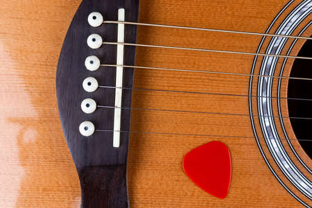 yellow guitar pick tucked into gold acoustic guitar strings on a dark wood fret board.の写真素材