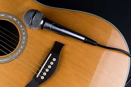 The neck of a classic six-string guitar and a silver microphone on a black background. guitar and accessories. creativity and playing the guitarの写真素材