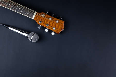 The neck of a classic six-string guitar and a silver microphone on a black background. guitar and accessories. creativity and playing the guitarの写真素材