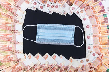 Russian money, rubles wrapped in a medical mask. Medical face masks and money. Surgical face mask. COVID-19 caused a shortage of face masks. Medical mask and five thousand rubles banknote on a black.の写真素材
