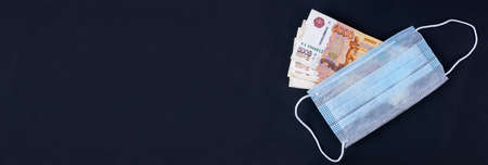 Russian money, rubles wrapped in a medical mask. Medical face masks and money. Surgical face mask. COVID-19 caused a shortage of face masks. Medical mask and five thousand rubles banknote on a black.の写真素材