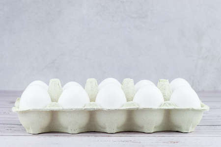 Close-up view of raw chicken eggs in an egg cell on a white wooden background