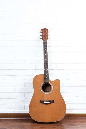 Musical instrument - acoustic guitar with cutaway on a white brick wall background.