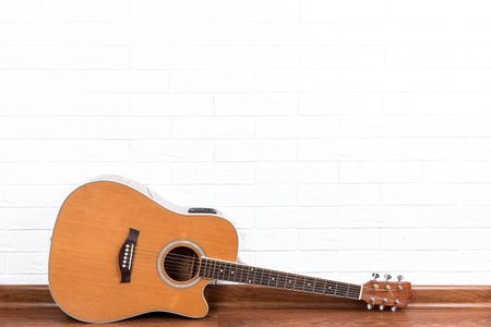 Musical instrument - acoustic guitar with cutaway on a white brick wall background.
