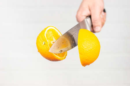 man cuts an orange in flight on a brick white wall backgroundの写真素材