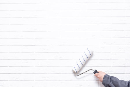 A man's hand with a roller paints the wall with white paint. Painting a white brick wallの写真素材