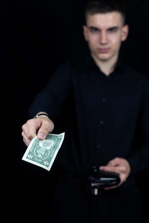 Young handsome man businessman with a dollar in his hands on a black background