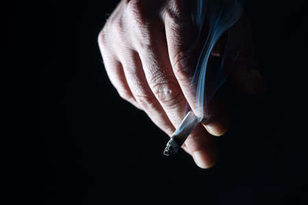 Hand holding cigarette on black background. Close-up of male hand holding cigarette isolated on dark background. Men smoke.の写真素材