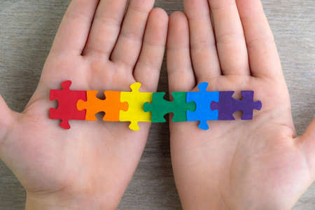 sex education in the spirit of equality and tolerance: a student builds a LGBT pride flag of the puzzle, short focus, top viewの写真素材