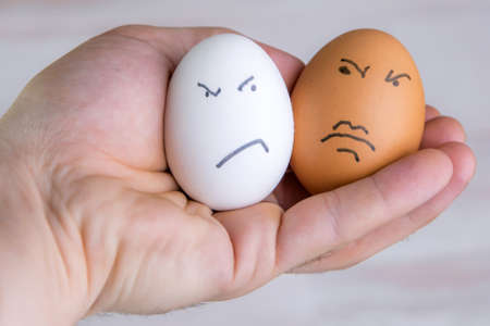 prejudices of racism: two eggs of different colors with dislike look at each other, short focus