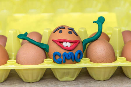 GMO: the joyful genetic monster-egg smiles happily and waving a hand among a variety of ordinary...