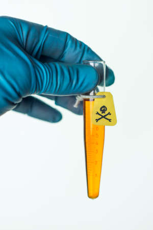 container with a poison in the scientist's hand, a yellow warning label with a skull and bones, on white, a short focusの写真素材