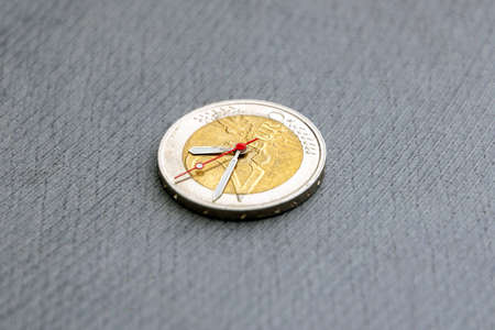 time to benefit: 2 euro coin with hour hands on a dark background, short focus, closeの写真素材