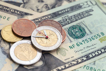exchange rate: 2 euro coin with hour hands on a pile of dollars, several different eurocents near,...