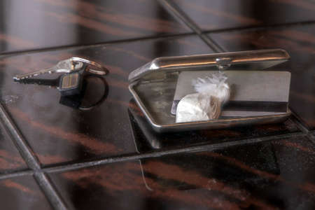 dose of cocaine in a plastic bag and a card inside an open cigarette case, a key in the background
