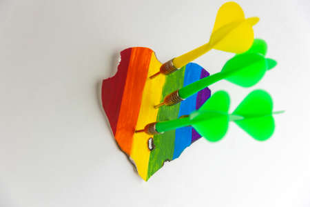 Concept - harassment of LGBT community freedom: burnt and torn rainbow heart pierced with darts, short focusの写真素材