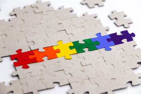 LGBT pride flag, built from a puzzle, among gray puzzles, short focus, on a white background, side viewの写真素材