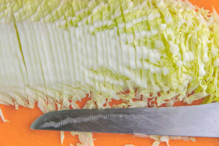 finely chopped Chinese cabbage on an orange board, a sharp knife next. Short focus, closeの写真素材