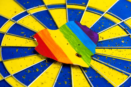 Concept - harassment of the freedom of the LGBT community: burned and torn rainbow heart pierced by darts, short focusの写真素材