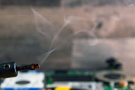 smoke from boiling rosin on a heated soldering iron, disassembled electronic apparatus in the background. selective focus, closeの写真素材