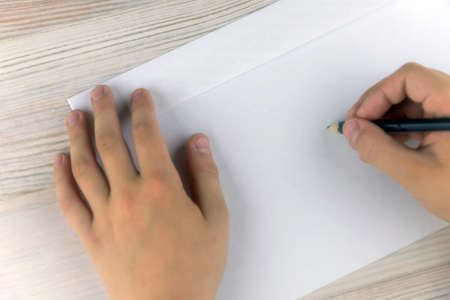 boy signs blank envelopes lying on a wooden table, close-up, low contrast, haze effectの写真素材