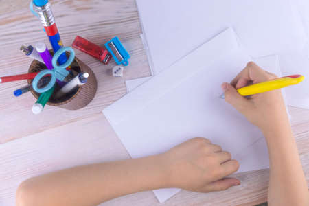boy signs blank envelopes lying on a wooden table, close-up, low contrast, haze effect