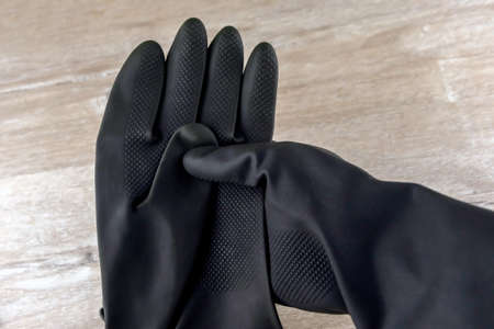 man removes black protective rubber gloves to work with caustic substances, on a light wooden...