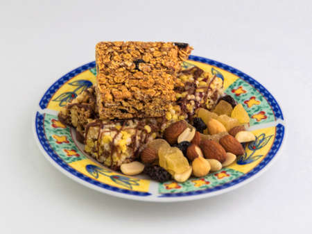 vegan dessert: several cereal bars with raisins and honey are on a bright plate, a lot of nuts and...