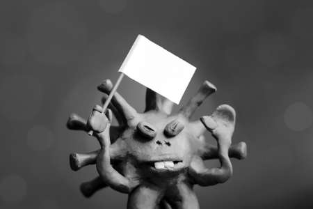 coronavirus COVID-19 defeated! Cartoon caricature of a virus surrenders, waving a white flag. Short focus, toning.の写真素材
