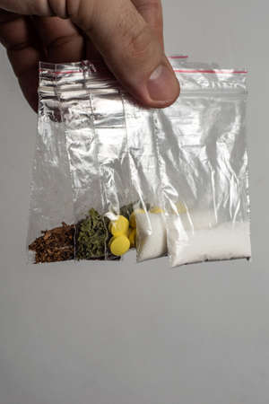 death row concept: tobacco, weed, MDMA tablets, amphetamine crystals, heroin in plastic bags, on a light background. Enhanced contrast, partial blur.の写真素材