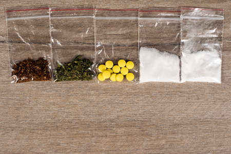 death row concept: tobacco, weed, MDMA tablets, amphetamine crystals, heroin in plastic bags, on a...