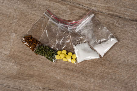 death row concept: tobacco, weed, MDMA tablets, amphetamine crystals, heroin in plastic bags, on a light background. Enhanced contrast, partial blur.の写真素材