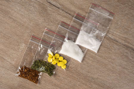 death row concept: tobacco, weed, MDMA tablets, amphetamine crystals, heroin in plastic bags, on a light background. Enhanced contrast, partial blur.の写真素材